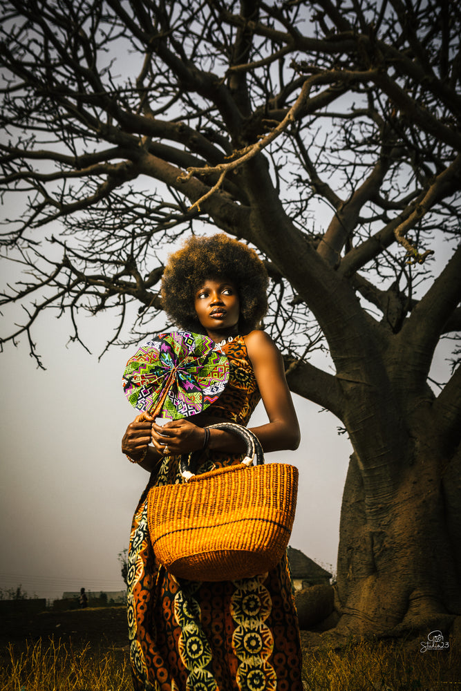 A woman wearing a vibrant African dress holds a woven basket, showcasing cultural attire and craftsmanship.