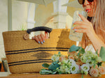 A woman seated at a table, casually holding a straw bag beside her, sipping lemonade and enjoying a moment of relaxation.